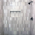 Shower wall with gray and white vertical stacked tile, recessed niche, and matte black shower head