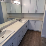 Long white shaker vanity with integrated sink, upper cabinets, and wood-look flooring