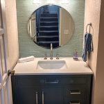 Powder room with navy vanity, white countertop, round mirror, and sea-glass tile backsplash