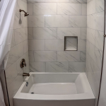 Alcove tub and shower with white marble-look tile surround and recessed niche