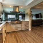 Kitchen peninsula with gas cooktop and stainless chimney hood, open to the family room through an arched doorway