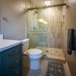 Glass-enclosed walk-in shower with vertical tile beside a green vanity and toilet in a San Diego bathroom remodel