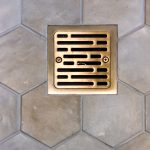 Brushed gold square shower drain set in large hexagon floor tile
