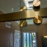 Close-up of brushed gold roller hardware on a sliding glass shower door