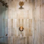 Brushed gold shower head and valve set against vertical stacked wall tile in a walk-in shower