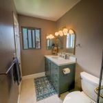 Second remodeled bathroom with green vanity, globe vanity lights, round mirrors, and a patterned rug