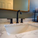 Undermount sink with marble-look countertop and matte black widespread faucet below a wood-framed mirror