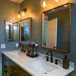 Double sink vanity with white countertop, matte black faucets, arched wood-framed mirrors, and brass wall sconces