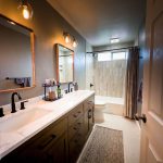 Remodeled Santee bathroom with dark double vanity, matte black faucets, wood-framed mirrors, and a tiled tub-shower beyond