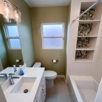 Remodeled La Mesa bathroom with sage green walls, white vanity, tub with built-in shelving niche, and a window over the toilet