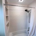 Tub and shower with white textured tile, built-in shelving niche, and handheld shower on a slide bar