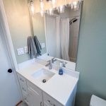 White vanity with single sink and chrome faucet under a wide mirror and vanity light in a San Diego bathroom remodel