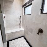 Curbless walk-in shower with large-format stone-look tile, handheld shower, and bronze valve