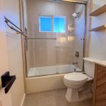 Tub and shower combo with sliding glass doors, tiled surround, and a window above in a remodeled bathroom