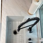Overhead view of a white single-bowl sink with stainless bottom grid and black coil pull-down faucet on a white countertop