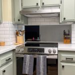 Stainless steel range with under-cabinet hood, subway tile backsplash, and sage green shaker cabinets in a San Diego kitchen