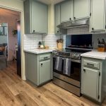 View through the doorway of a sage green kitchen with stainless range, white counters, and wood-look plank flooring