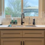 Undermount sink with matte black gooseneck faucet, white quartz countertop, and tile backsplash below a garden-view window
